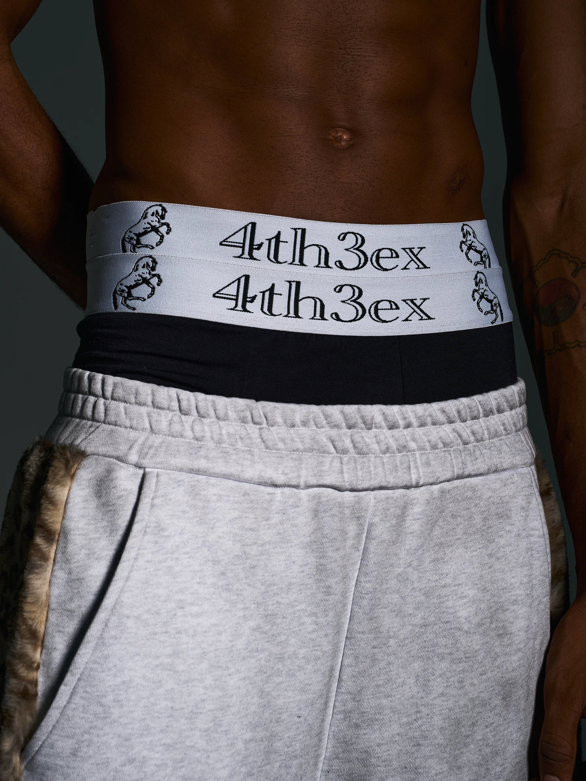 Double white waistband of boxer briefs styled above gray trousers